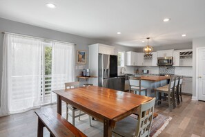 A modern kitchen with white cabinets, stainless steel appliances, and a wooden dining table. - Spoon Haven: Village at Nags Head | Sound Access (Nags Head)