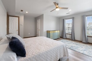 A bedroom with a bed, a ceiling fan, a dresser, and a window with curtains. - Spoon Haven: Village at Nags Head | Sound Access (Nags Head)