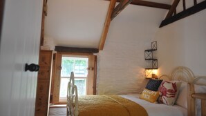 Un dormitorio con cama, vigas de madera, ventana y lámpara fijada a la pared.