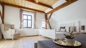 A bedroom with a sloped ceiling, a bed with a quilted cover, a bedside table with a tray, a radiator, a window with curtains, a chair, and a sofa. - Rudnik Krc070 in Rudn k (Rudník)