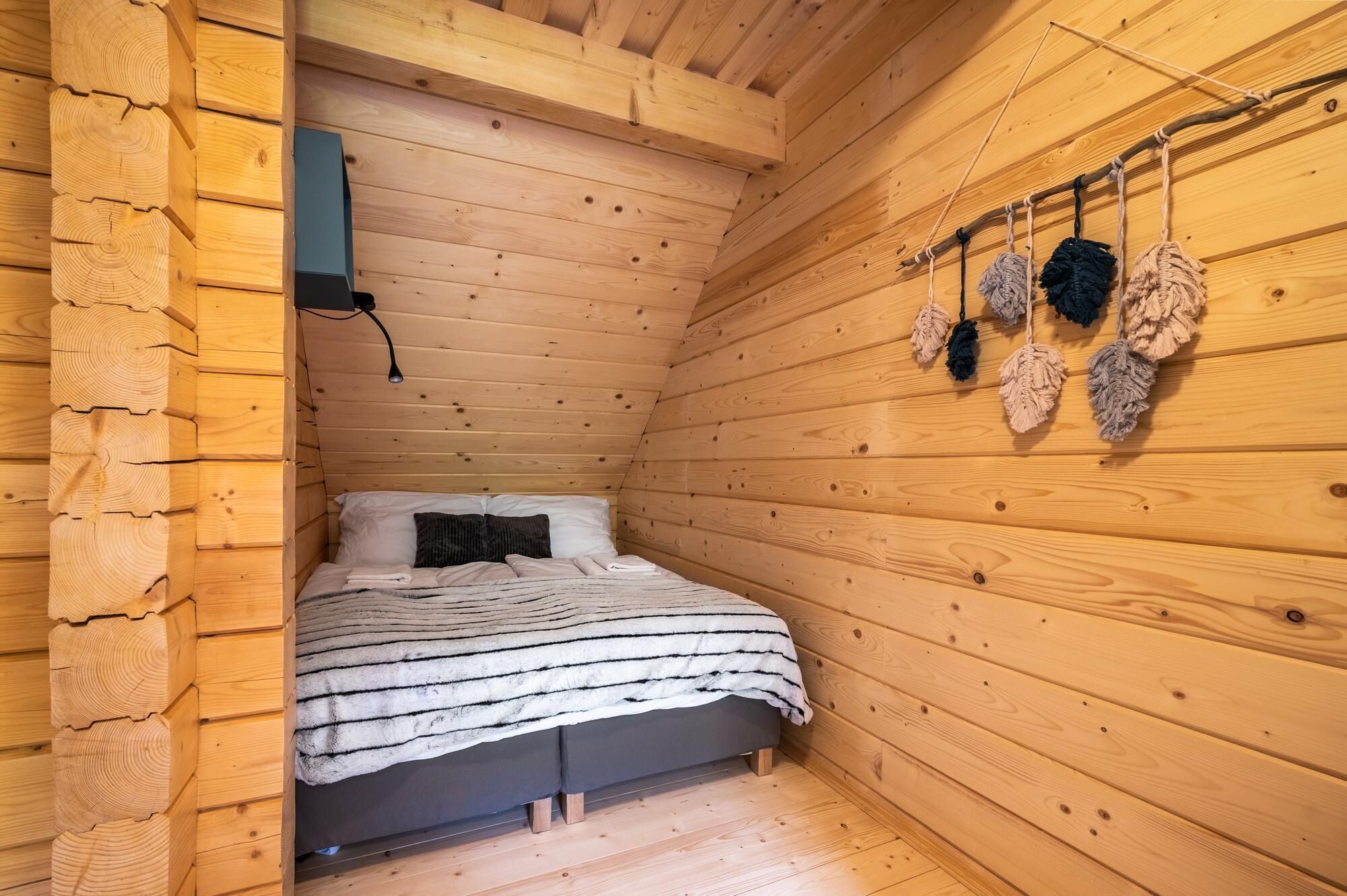 A cozy wooden cabin room with a bed, a hanging light fixture, and a wall-mounted heater.