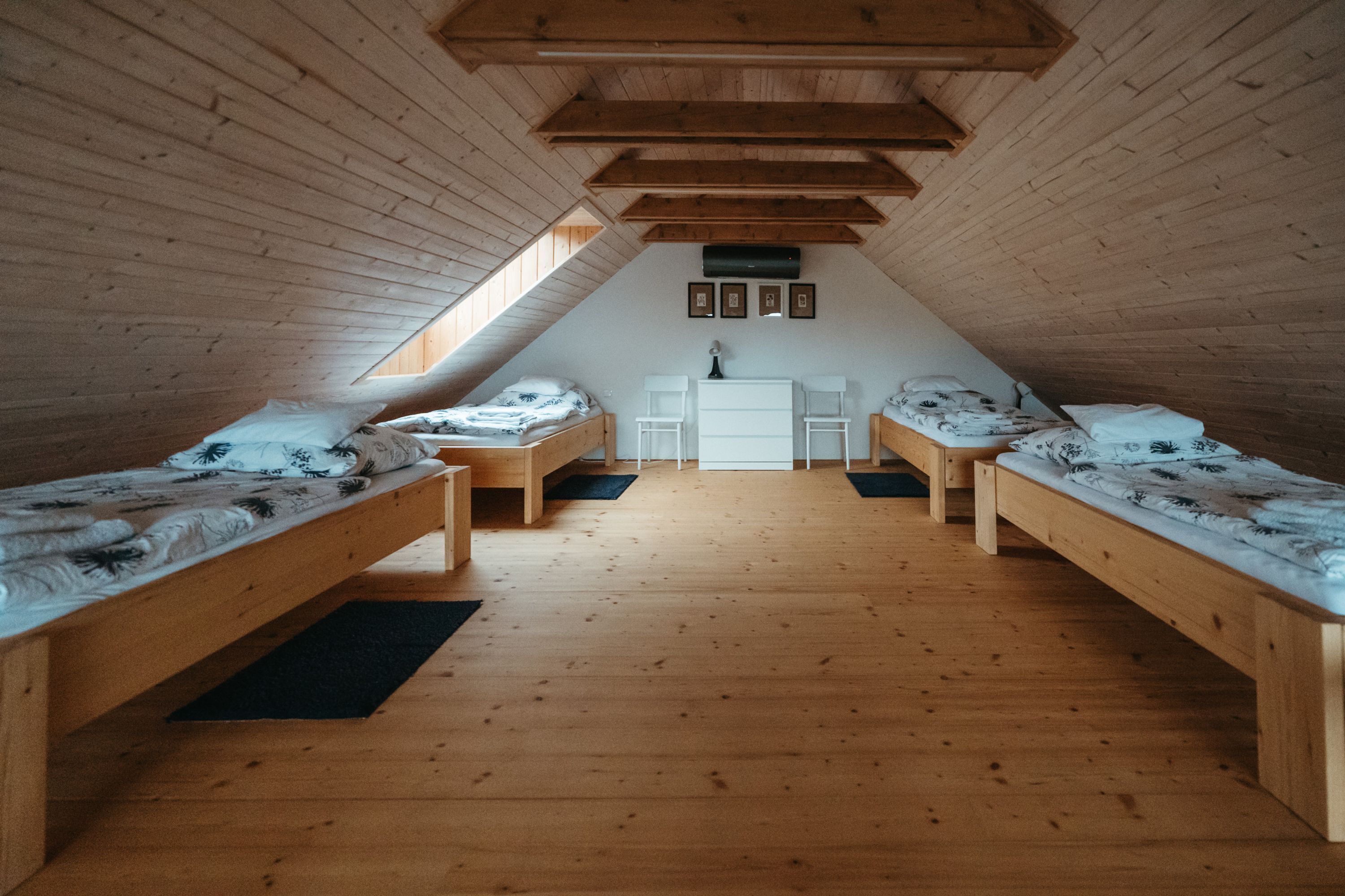 A room with three wooden beds arranged in a U-shape, a white door, and a small window.