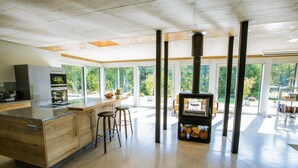 Una cocina moderna con una isla central, taburetes de bar, horno empotrado y ventanas grandes con vistas al exterior.