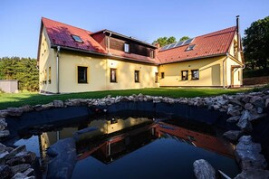 Um edifício grande e amarelo com telhado vermelho e um lago em primeiro plano.