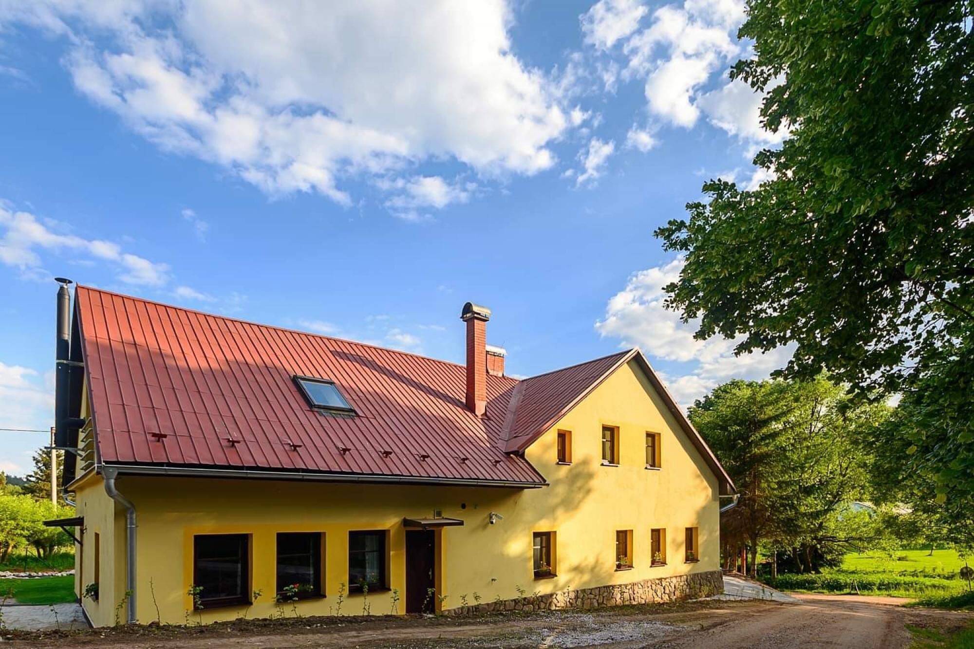 A yellow building with a red roof, a chimney, and a small window.
