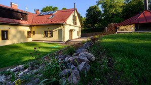 A two-story house with a sloped roof, a chimney, and a garden with a stone border. - Luxe Villa in Bernartice Kkh045 (Bernartice)