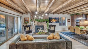Una sala de estar moderna con chimenea de piedra, sofá de cuero, comedor y una cocina visible a través de una puerta abierta.