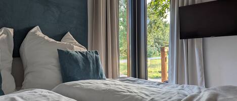 A bedroom with a bed, pillows, a TV, and a window with curtains.