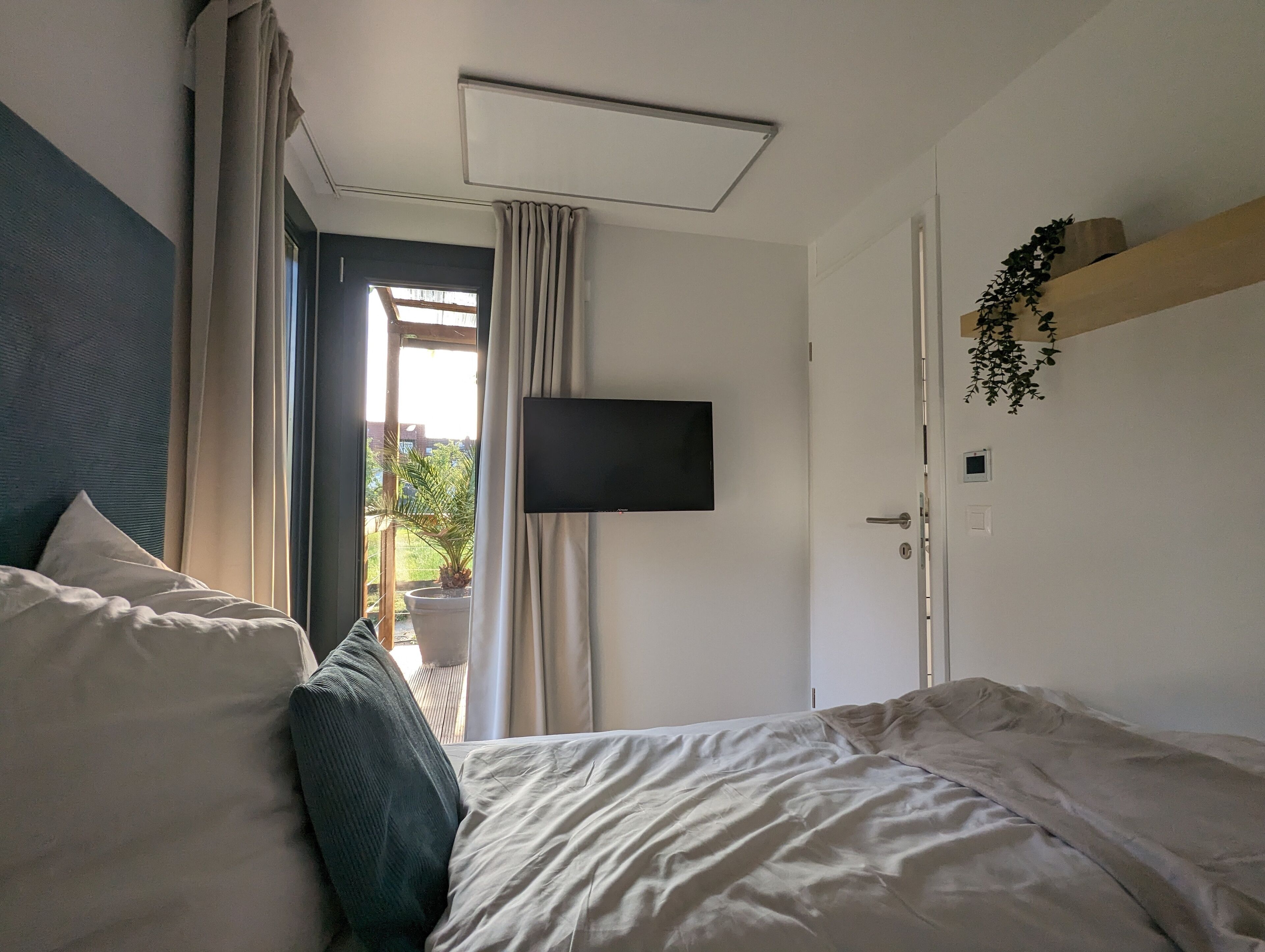 A bedroom with a bed, a TV mounted on the wall, a door, and a window with curtains.