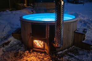 Un jacuzzi de madera con luz azul, rodeado de nieve.