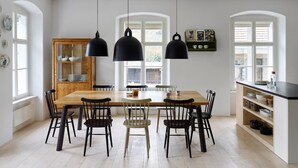 Comedor con mesa y sillas de madera, lámparas colgantes negras y un armario con vajilla.