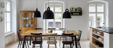 Comedor con mesa y sillas de madera, lámparas colgantes negras y un armario con vajilla.