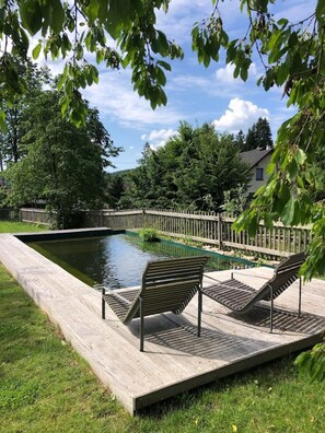 Relax by the serene pool surrounded by lush greenery and a wooden deck.