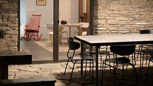 Comedor con suelo de piedra, una mesa, sillas y una lámpara colgante. Una silla es roja.