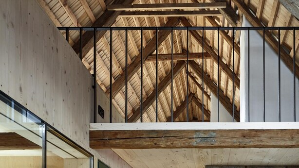 Un interior moderno con techo alto, vigas de madera y un corredor central que lleva a una habitación con cama.