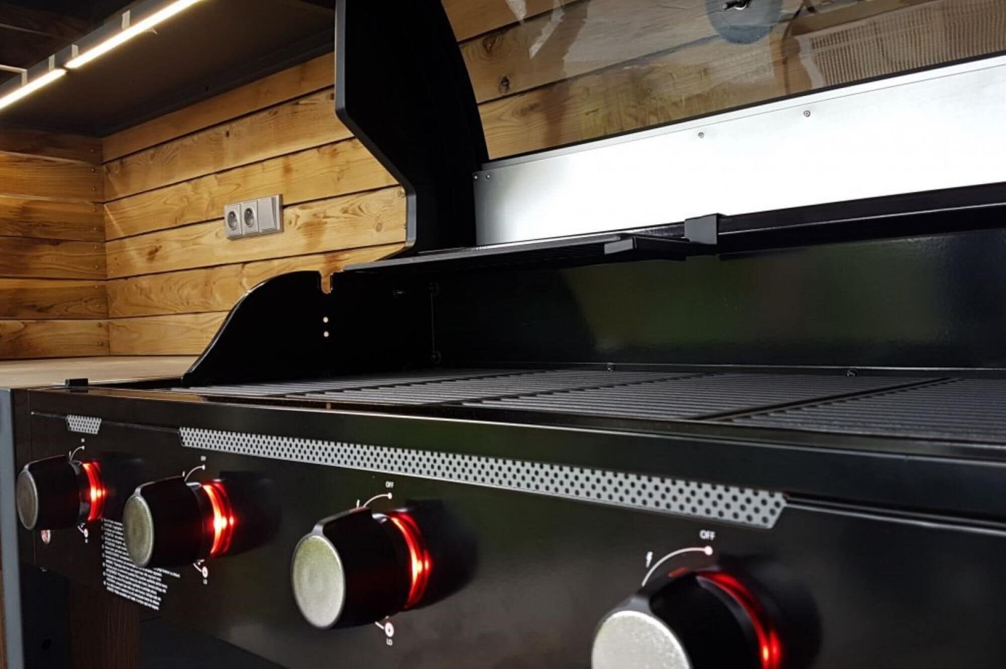 Une cuisinière en acier inoxydable dotée de quatre brûleurs et d’une plaque de cuisson, placée devant un mur en bois.