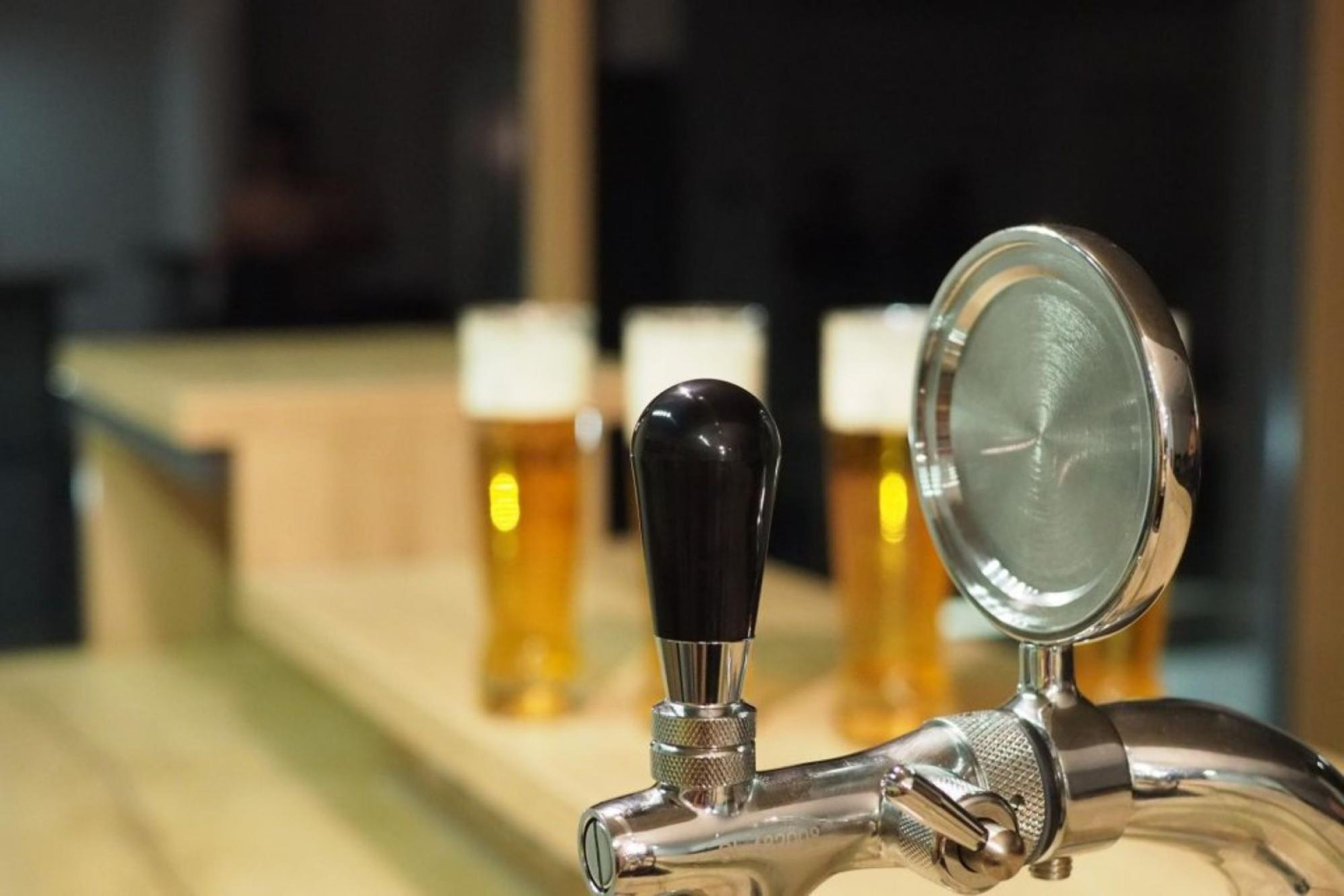 Uma torneira com um copo de cerveja preso e três garrafas de cerveja ao fundo.