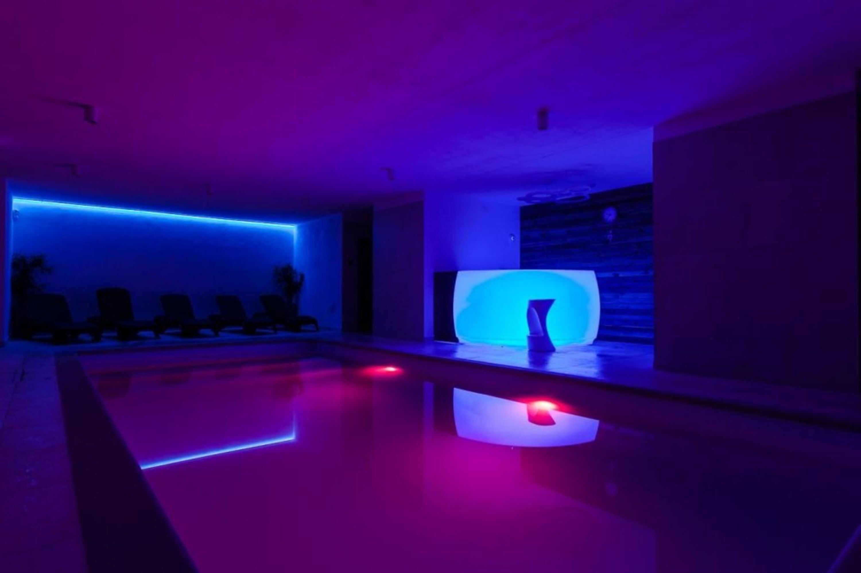 A modern indoor pool area with blue ambient lighting and a central illuminated structure.