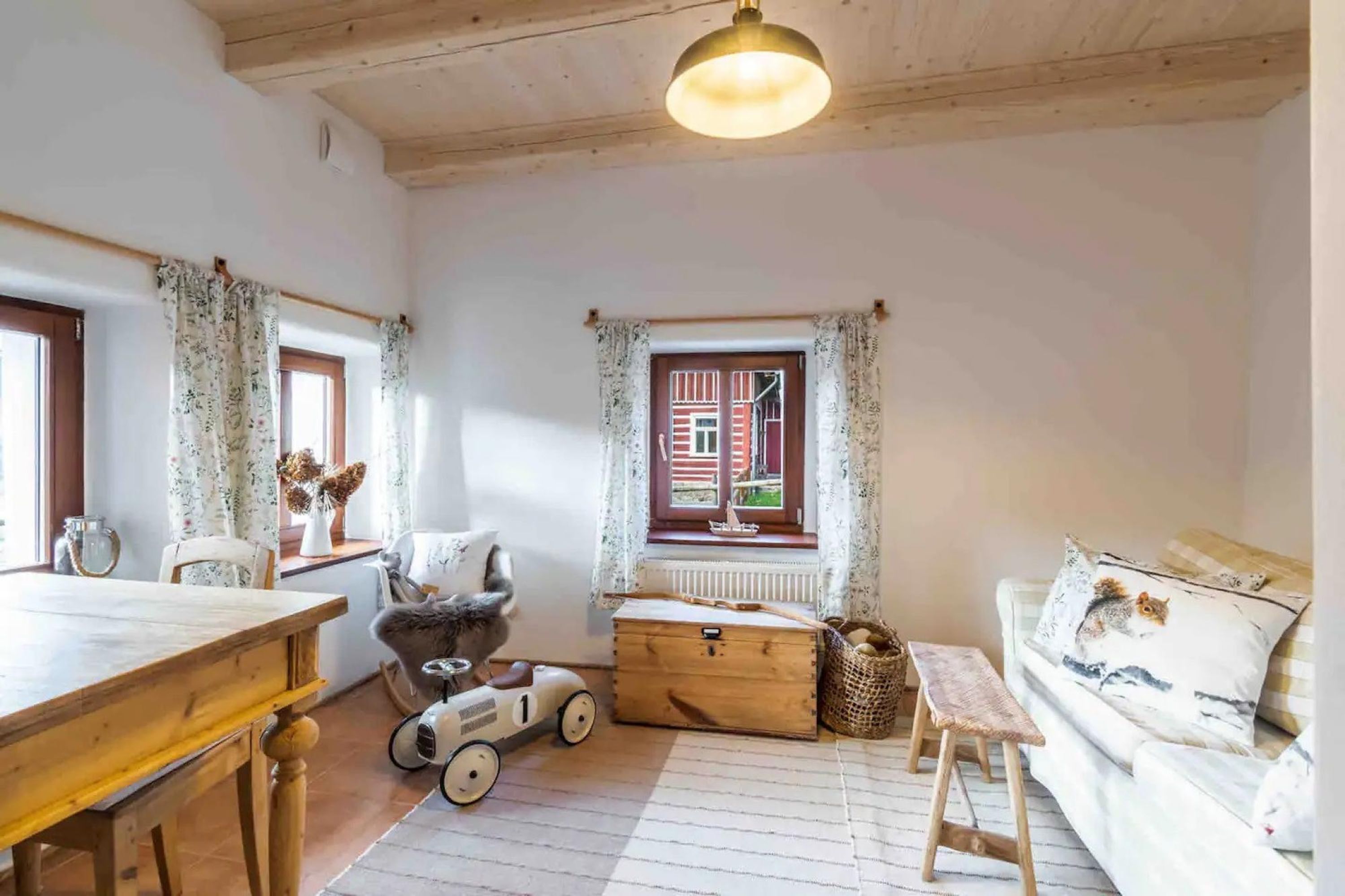 A cozy room with a wooden table, a sofa, a window with curtains, a radiator, and a toy car.