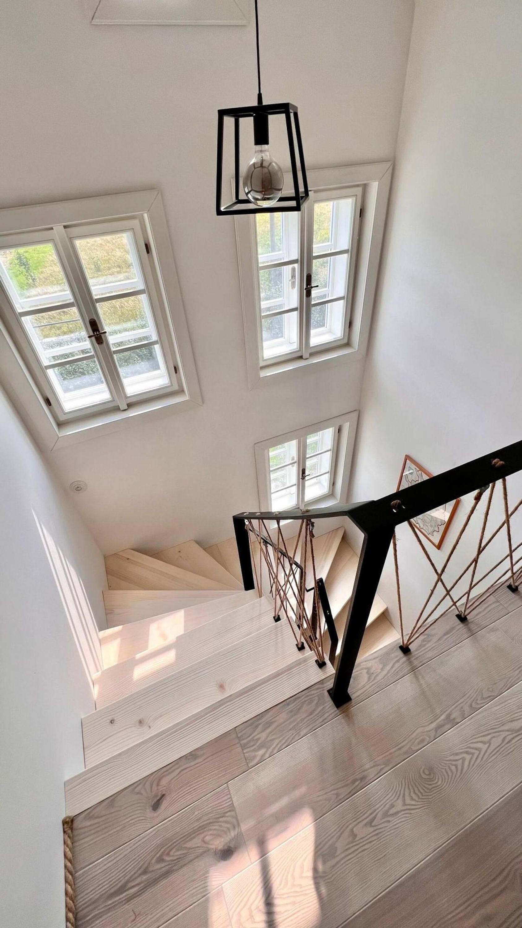 A staircase with wooden steps and a black metal railing, leading to a landing with a black pendant light.