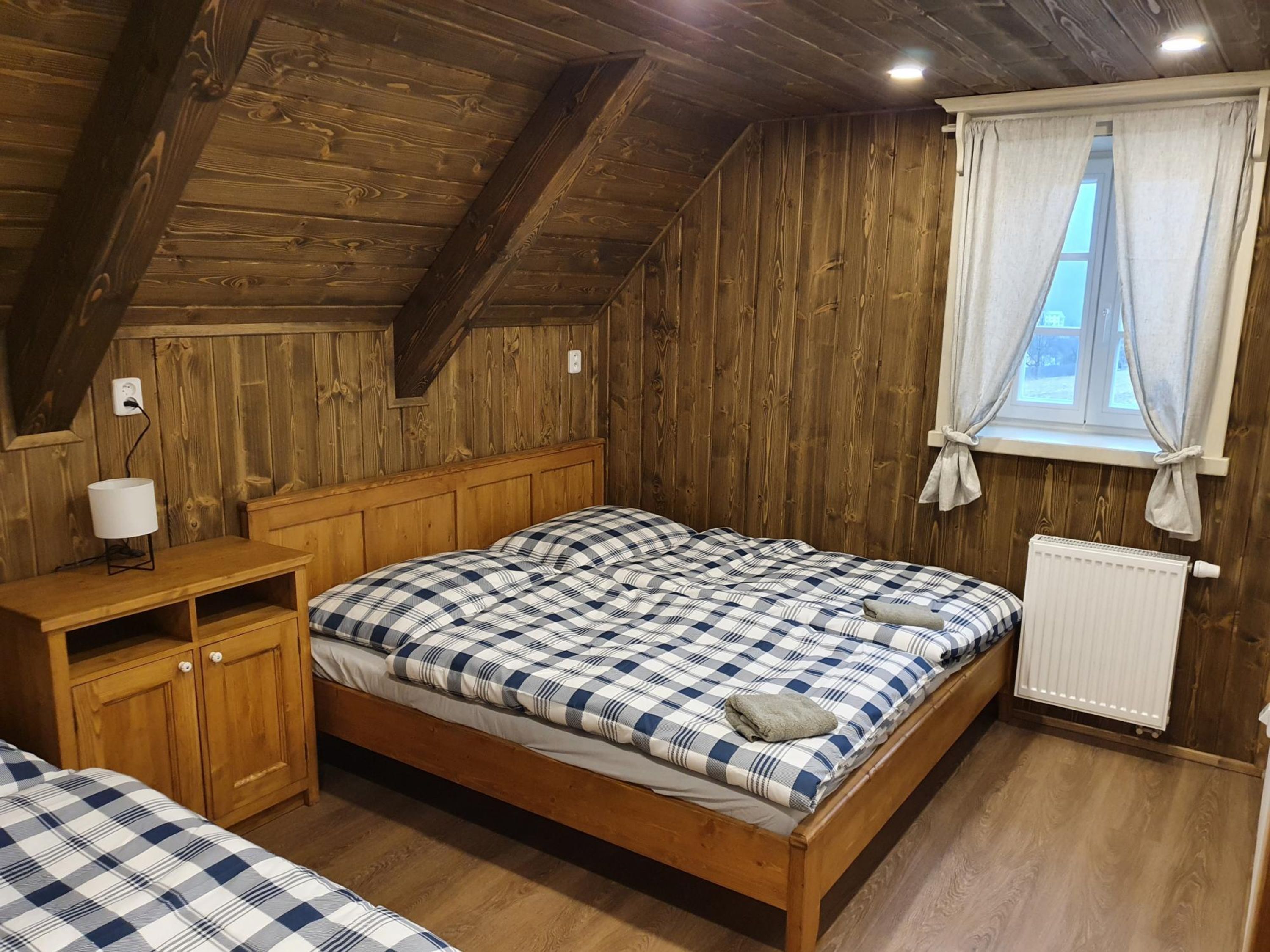 Ett mysigt rum med träpanel, en säng, ett litet träskåp och ett fönster med gardiner.