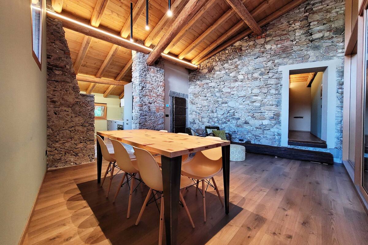 A rustic interior with a wooden table and chairs, stone walls, and exposed wooden beams.