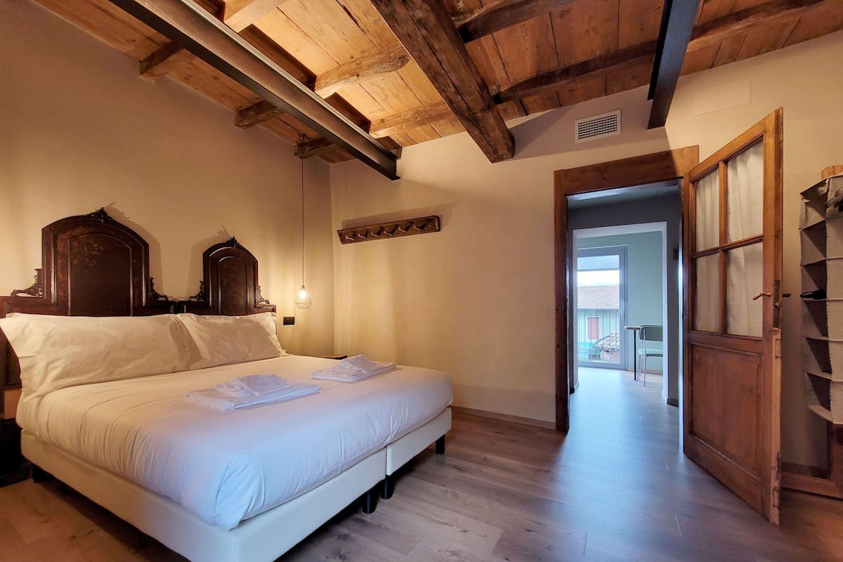 A bedroom with a wooden ceiling, a bed with white linens, a wooden wardrobe, and a view of the outside.