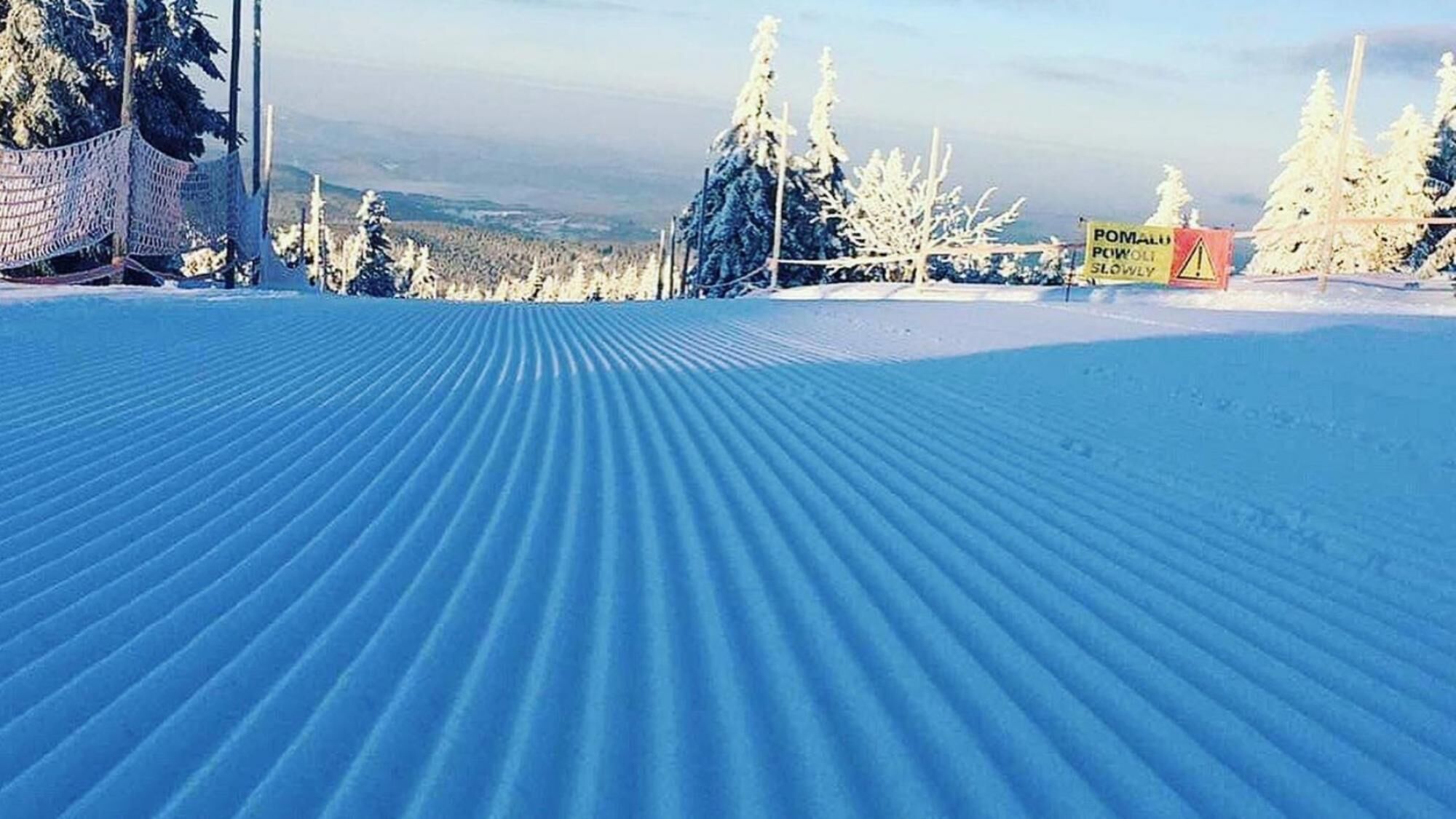 A snow-covered ski slope with a marked path and a sign indicating a slow area.