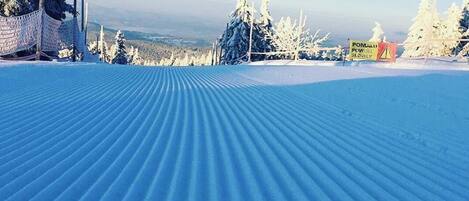 A snow-covered ski slope with a marked path and a sign indicating a slow area.
