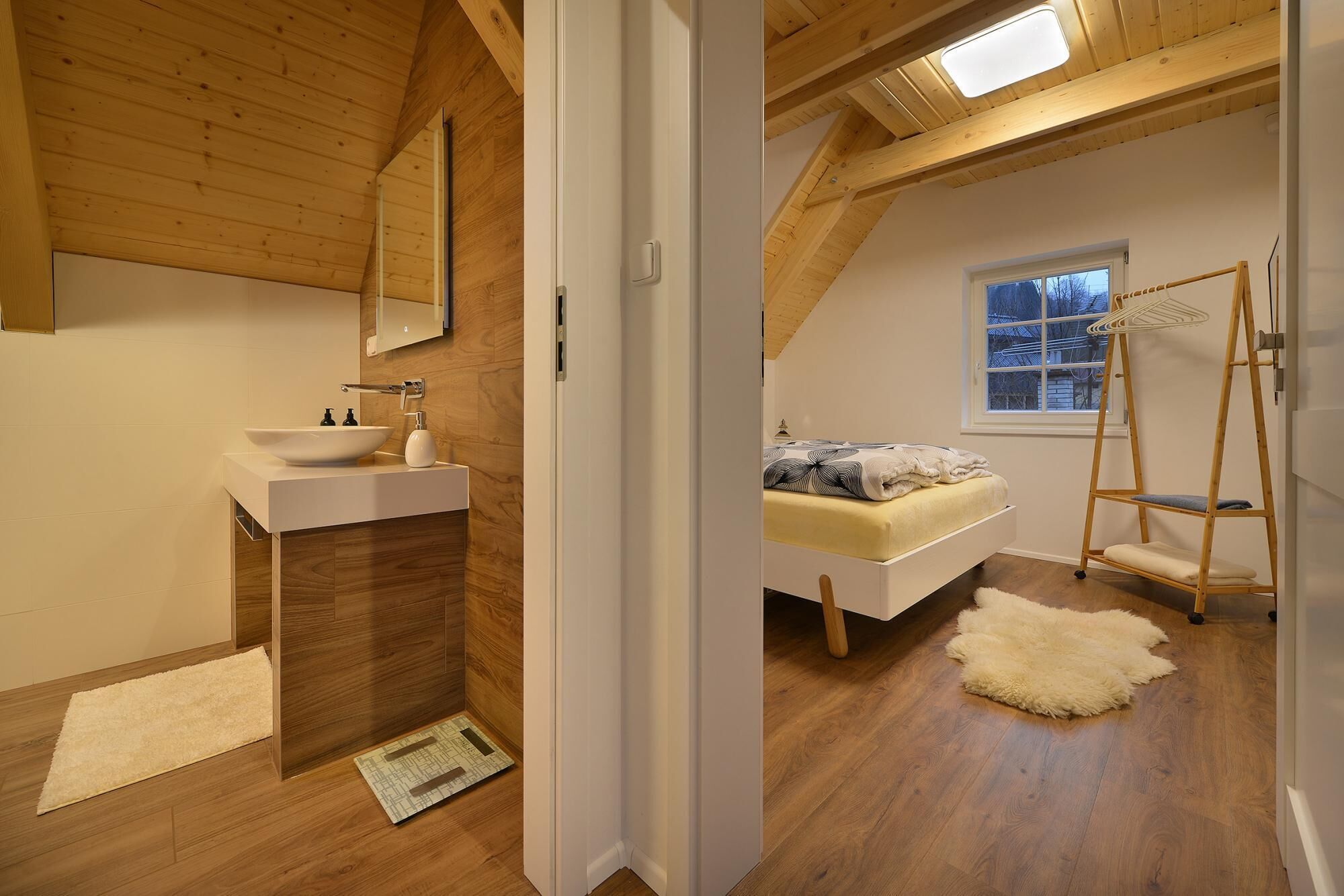 A bedroom with a bed, a ladder, a window, and a wooden ceiling.