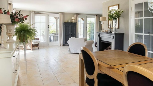 A spacious dining area with a wooden table and chairs, a fireplace, and a view through large windows. - Cozy cottage with heated pool, garden and covered terrace (Tzummarum)