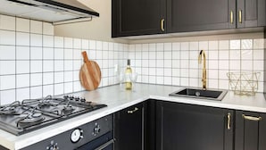 A modern kitchen with black cabinets, a white tiled backsplash, a gas stove, and a stainless steel sink. - Cozy cottage with heated pool, garden and covered terrace (Tzummarum)