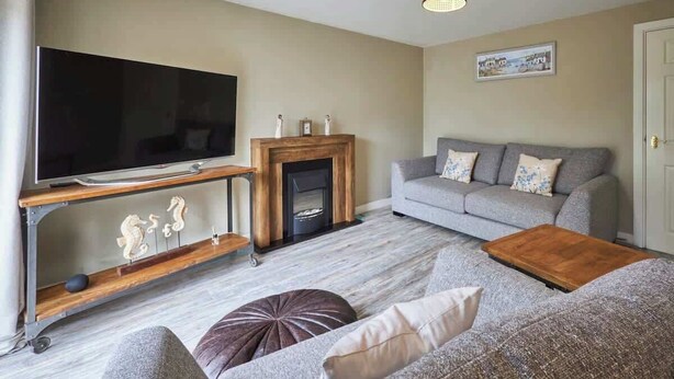 Ein Wohnzimmer mit Flachbildfernseher, Kamin, grauem Sofa und Couchtisch aus Holz.