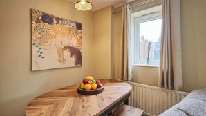 Ein Zimmer mit Holztisch, Obstschale, Gemälde, Fenster und Heizkörper.