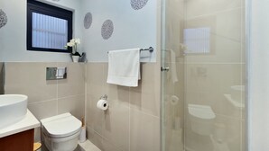 A modern bathroom with a toilet, sink, and glass shower enclosure. - Eden on the Bay 129 (Cape Town)