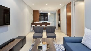 A modern living room with a blue sofa, two grey armchairs, a coffee table, and a TV mounted on the wall. - Eden on the Bay 129 (Cape Town)
