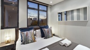 A modern hotel room with a large bed, a bedside table with a lamp, and a window with a city view. - Eden on the Bay 129 (Cape Town)