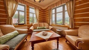 A cozy log cabin room with a wooden floor, a central table with a bowl of snacks, two sofas, and large windows offering a forest view. - Albrechtice Lat085 in Albrechtice v Jizersk ch hor ch (Albrechtice v Jizerských horách)
