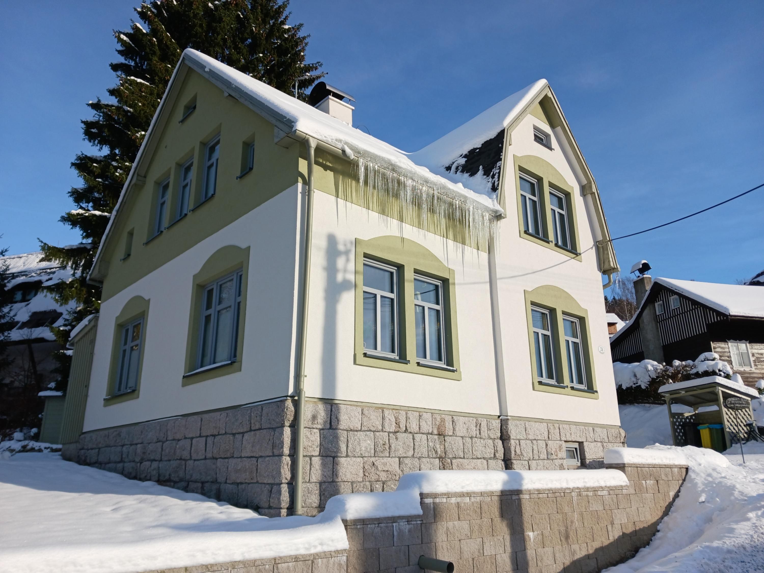 Una casa de dos pisos con base de piedra, varias ventanas y techo cubierto de nieve.
