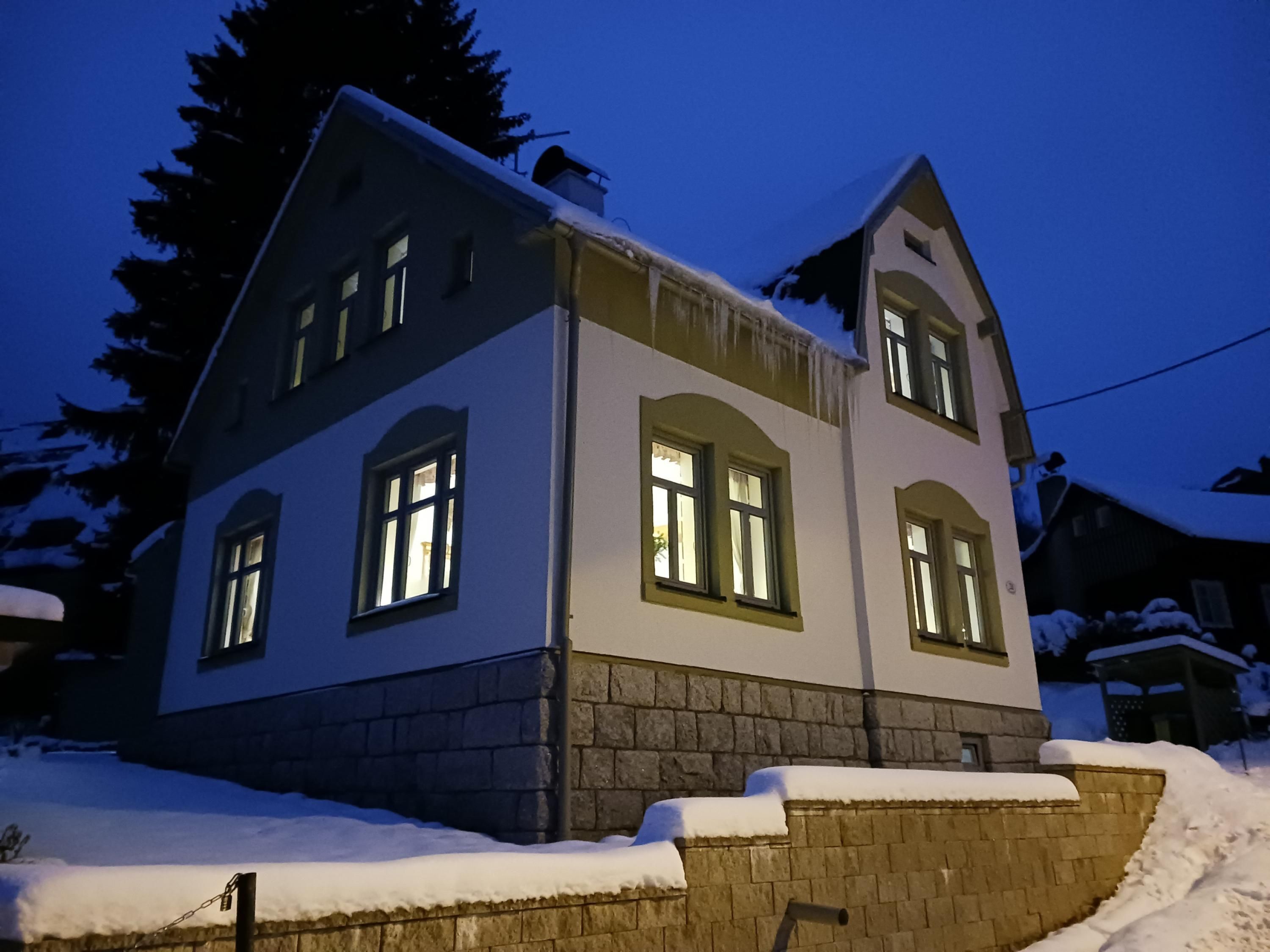 A two-story house with a stone foundation and snow-covered roof.
