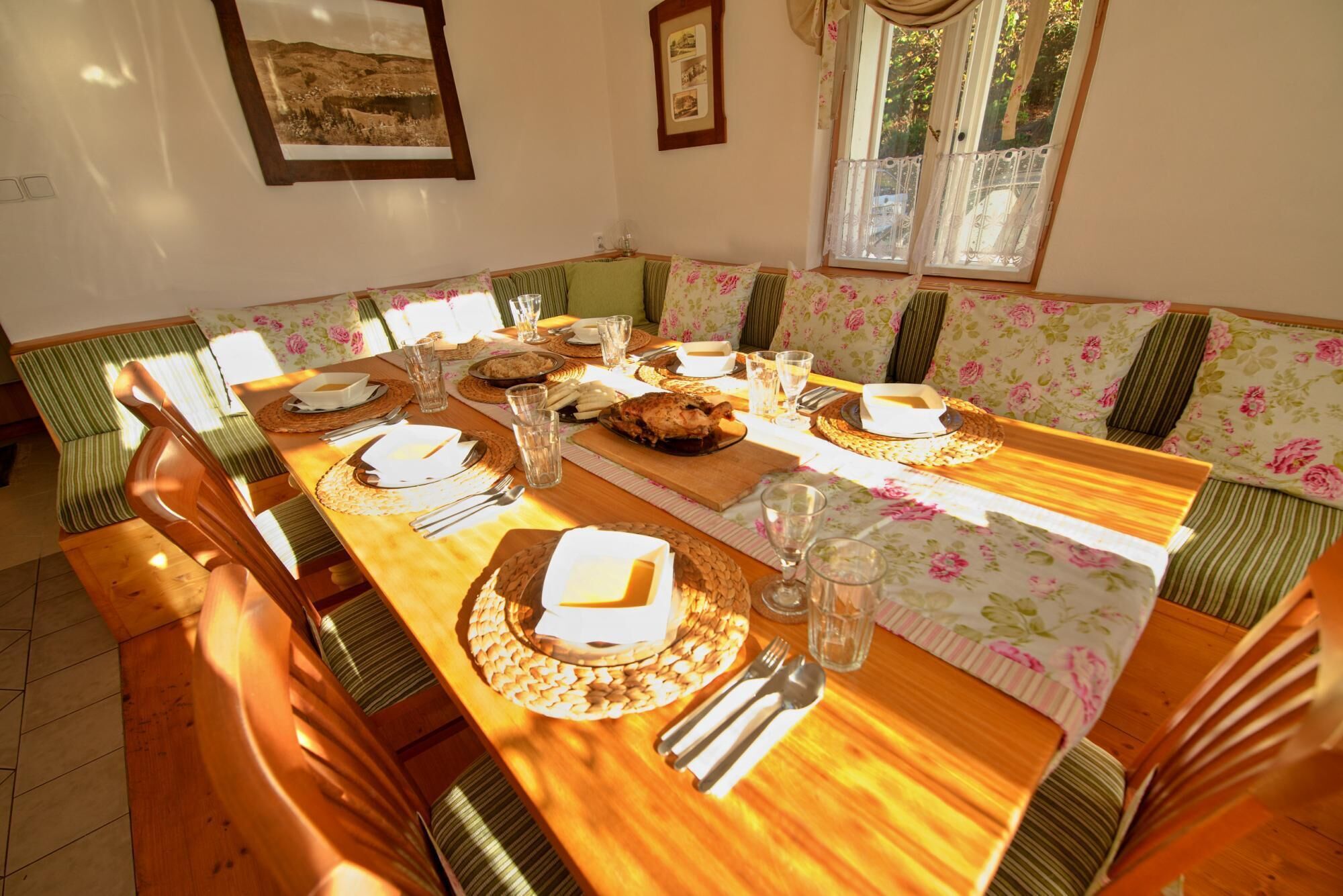 A dining area with a wooden table set for four, surrounded by striped green and floral patterned benches.