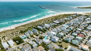 Vue aérienne d’une zone résidentielle côtière, avec des maisons, une plage et une jetée.
