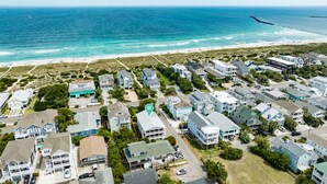Vue aérienne d’une zone résidentielle côtière, avec des maisons, une plage et une jetée.