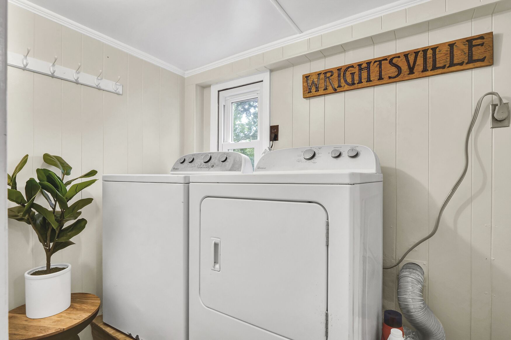 A laundry room with a white washer and dryer, a plant, a sign reading "Wrightsville," and a window.