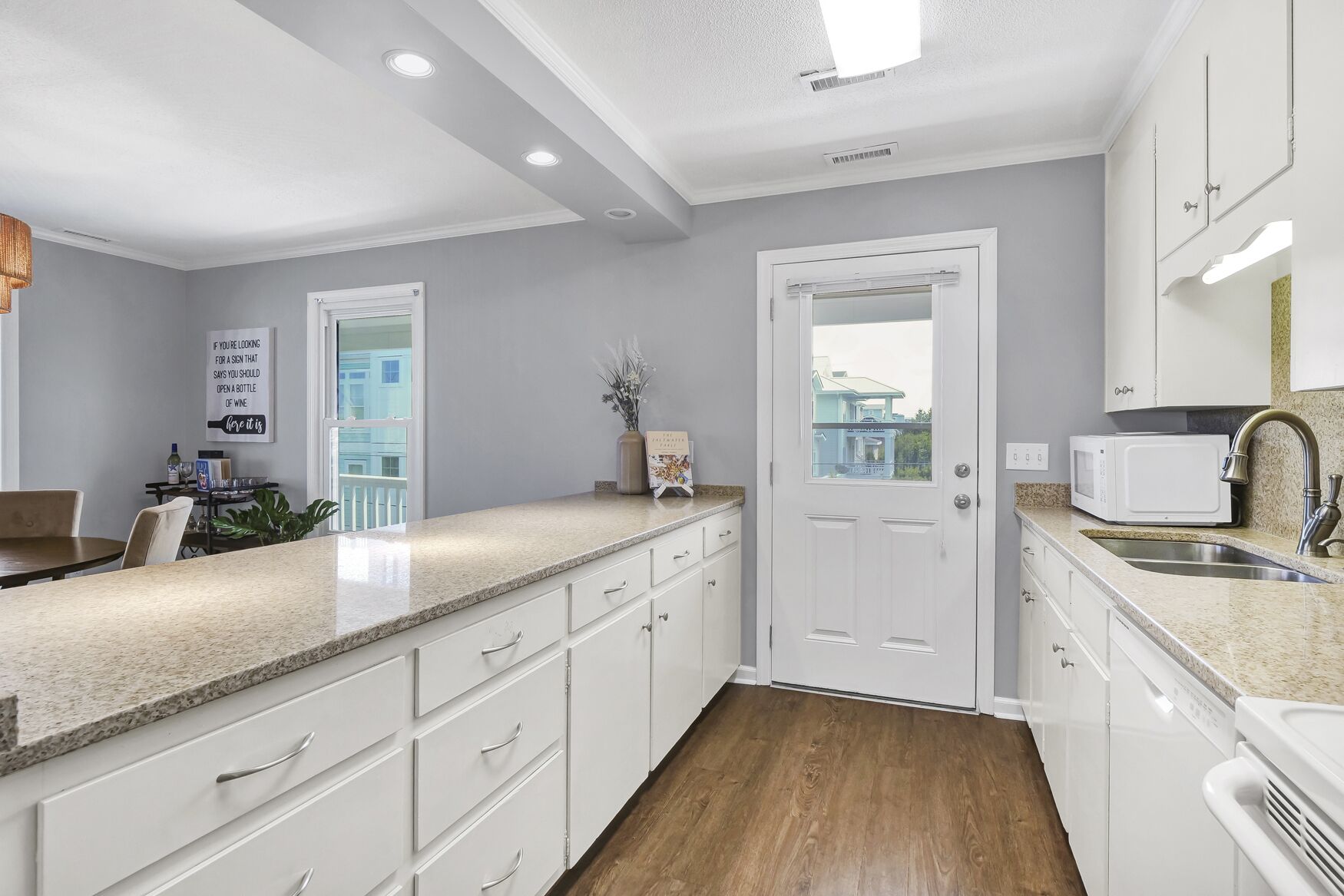 A modern kitchen with white cabinetry, a granite countertop, a built-in microwave, a sink, and a view of the outside through a door.