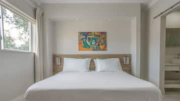 Quarto de hotel moderno com uma cama grande, uma pintura abstrata colorida acima dela e vista para o banheiro por uma porta aberta.