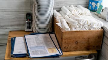 Une table en bois sur laquelle sont empilées des assiettes blanches, des serviettes blanches pliées et un menu.
