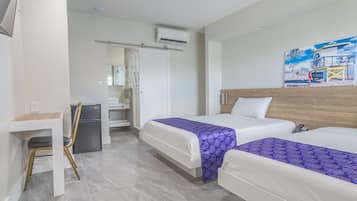 Habitación de hotel con dos camas, un escritorio, una silla, un refrigerador y un baño con ducha e inodoro.