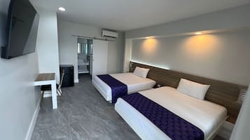 Two single beds with white linens and a dark blue bedspread, a flat-screen TV, and a small desk with a chair.