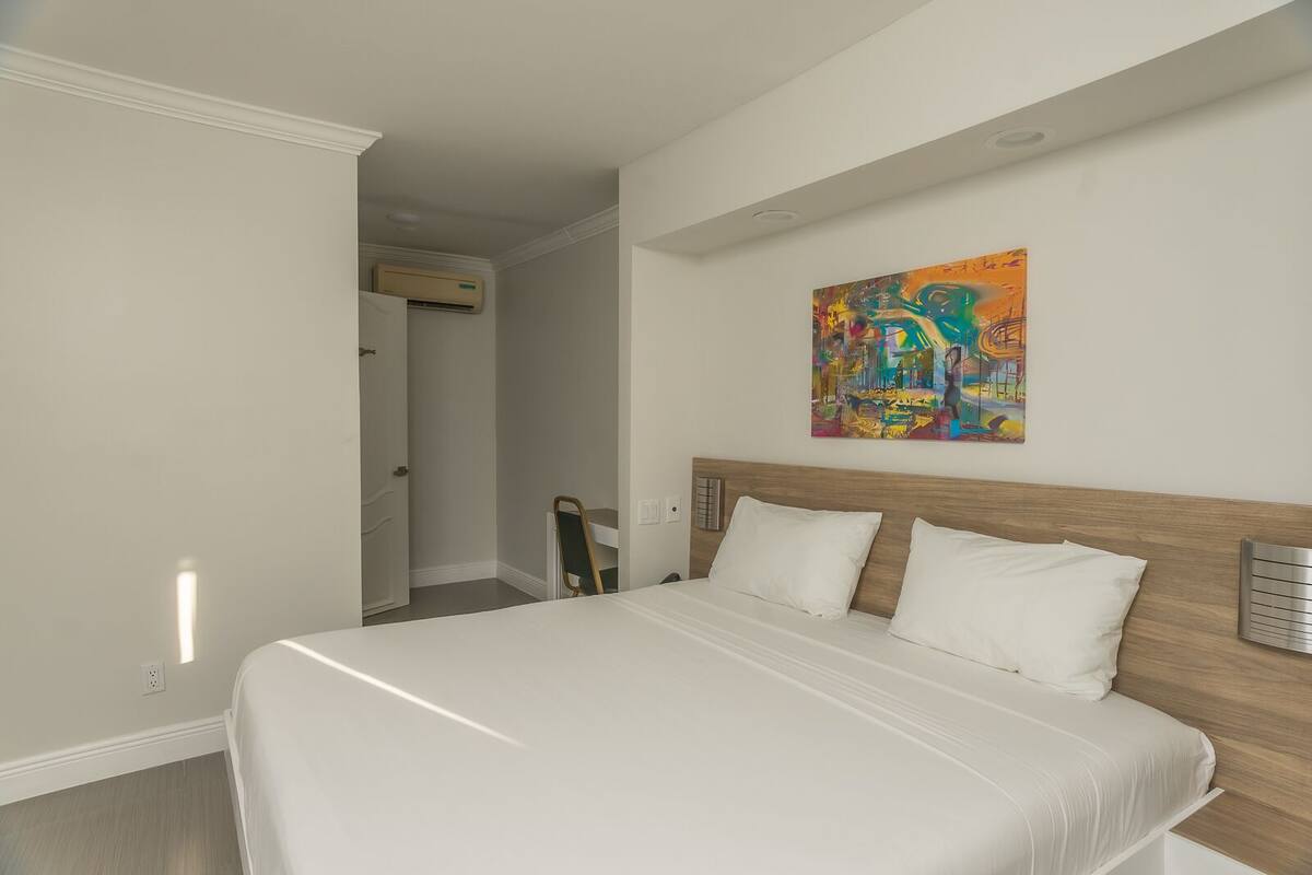 Um quarto com uma cama grande, cabeceira de madeira e um quadro abstrato colorido na parede.